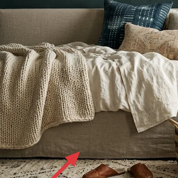 A patterned area rug on a wooden floor, partially visible under a bed, with a woven basket and slippers.