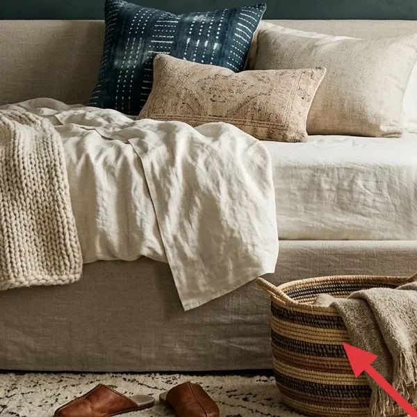 A striped woven basket with a soft, natural-toned throw blanket inside, sitting on a patterned area rug.