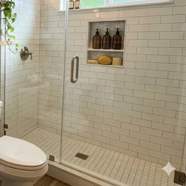 A recessed shower niche with white hexagonal tiles, holding three amber pump bottles, a natural sea sponge, and a bar of soap, set against white subway tiles.
